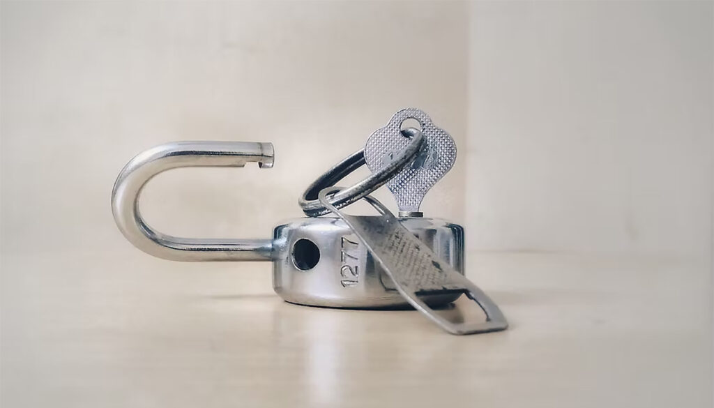Open metal padlock lying on a flat surface with keys still attached.