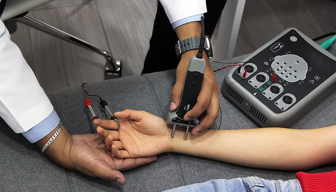Clinician performing a nerve conduction test on a patient’s forearm using handheld electrodes connected to a monitoring device.