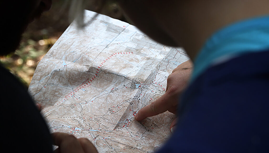 Two people reviewing a folded road map outdoors, pointing at a route while planning a trip.