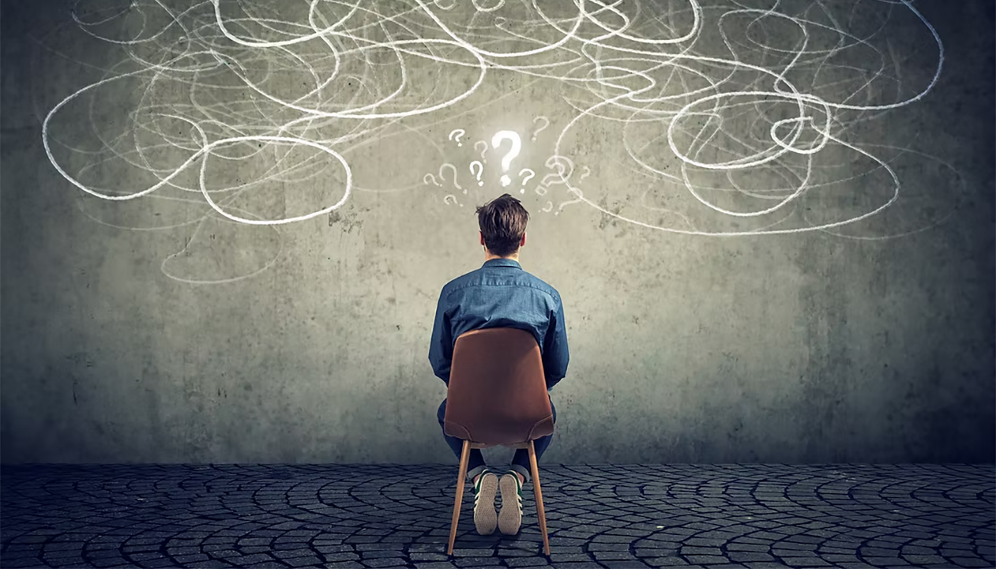 Person sitting on a chair facing a wall covered with chalk-like lines and question marks.
